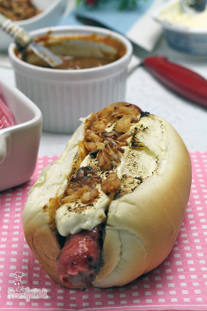 Sanduíche estilo food truck feito com linguiça defumada, molho barbecue de tomate pelado, cream cheese maçaricado no pão de cachorro-quente com cebola crocante (crispy).