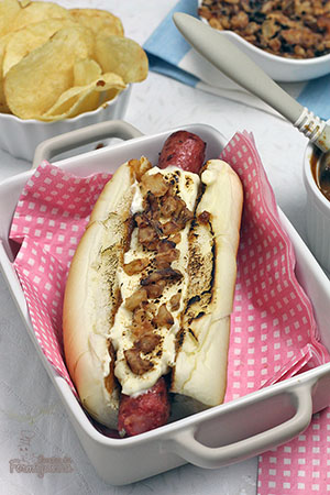 Sanduíche estilo food truck feito com linguiça defumada, molho barbecue de tomate pelado, cream cheese maçaricado no pão de cachorro-quente com cebola crocante (crispy).